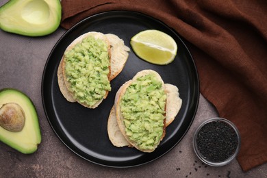 Photo of Delicious sandwiches with guacamole, avocados and black sesame seeds on brown table, flat lay