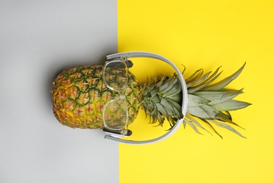 Fresh pineapple with headphones and glasses on color background, top view