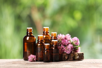 Bottles with essential oil and clover flowers on wooden table against blurred green background. Space for text