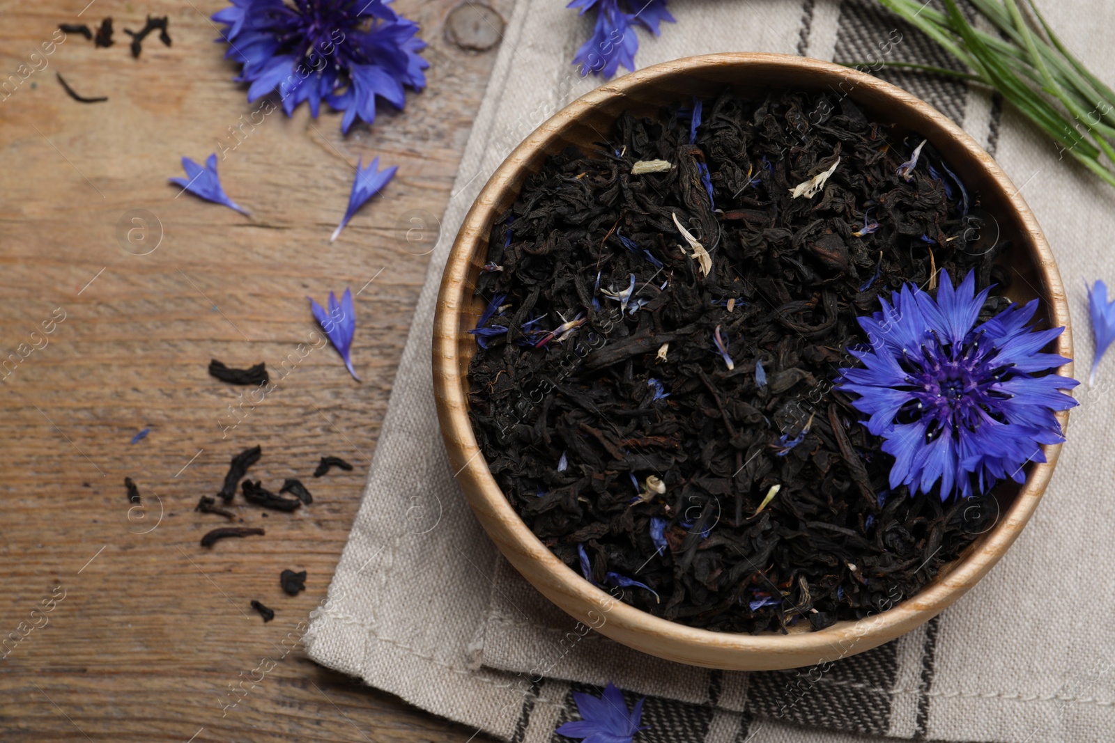 Photo of Dried cornflower tea and fresh flowers on wooden table, above view