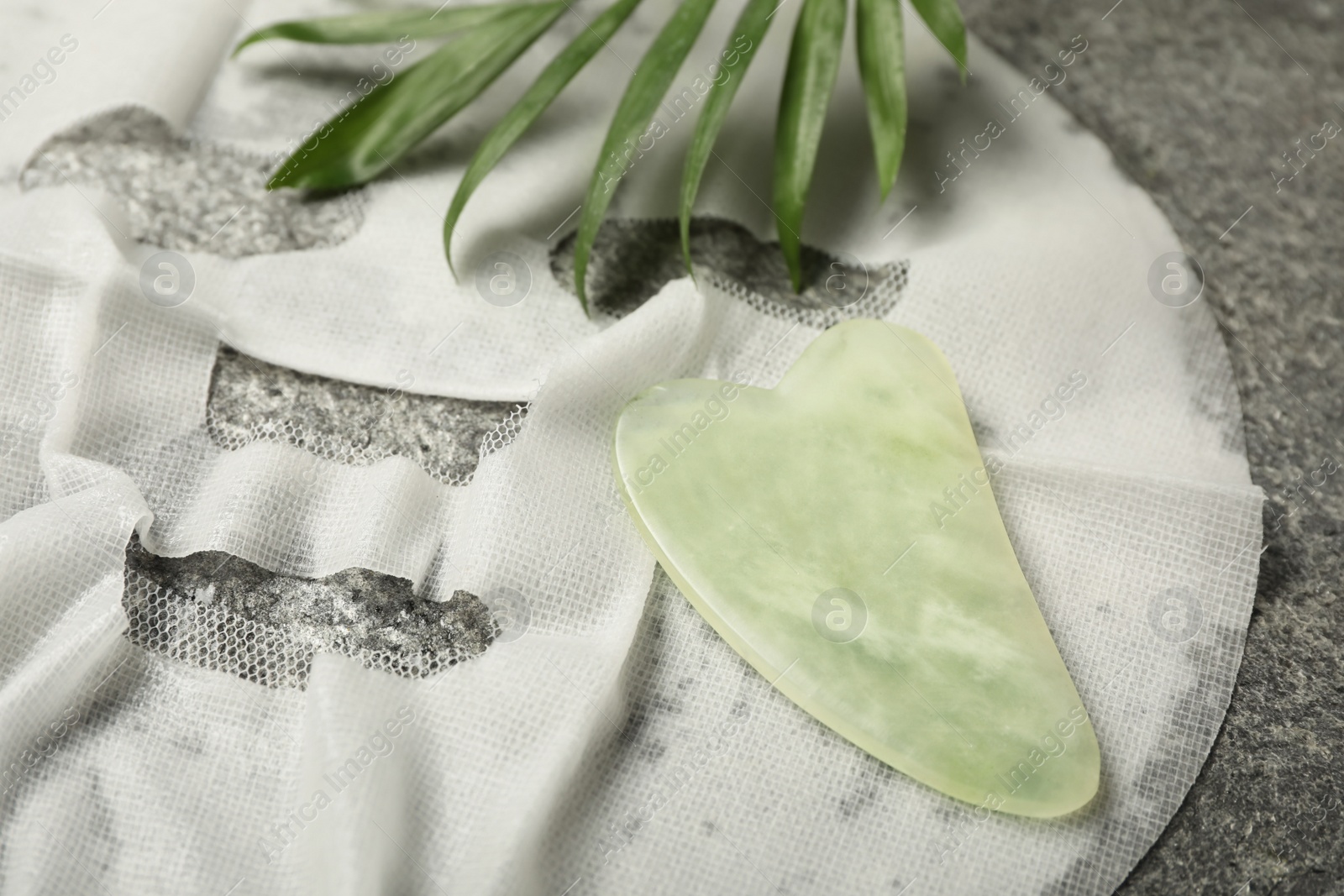 Photo of Jade gua sha tool and facial mask on grey table