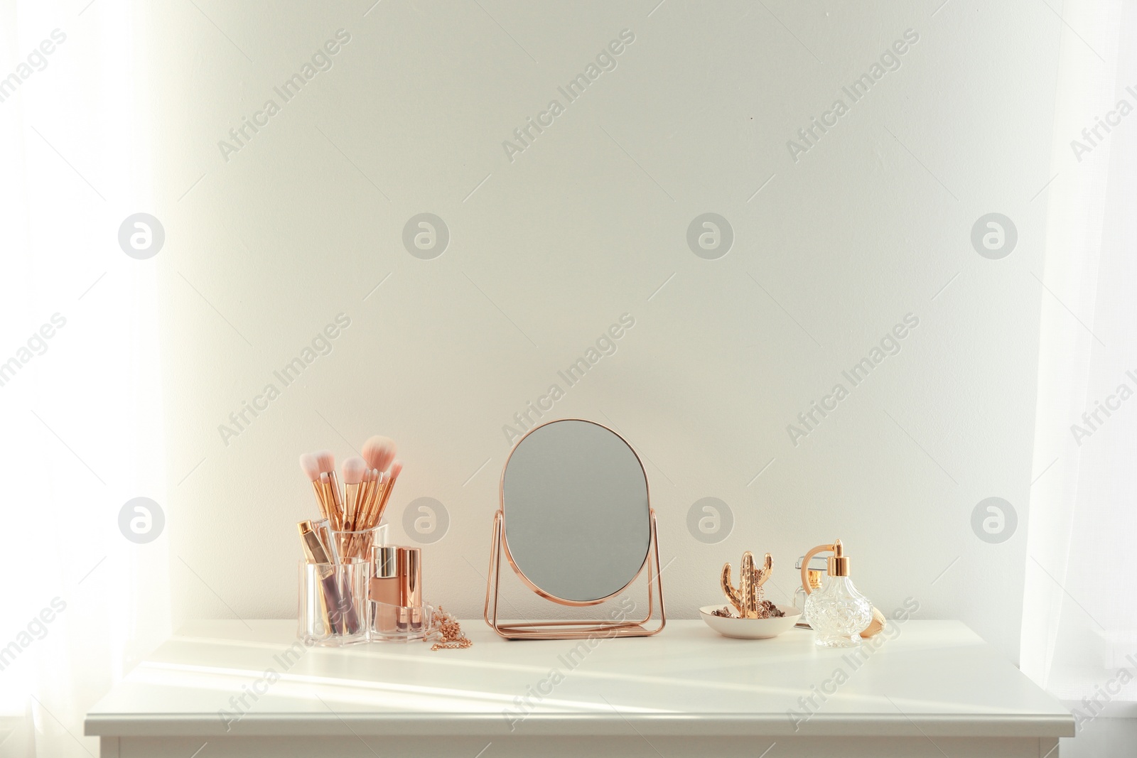Photo of Small mirror and  makeup products on white dressing table indoors