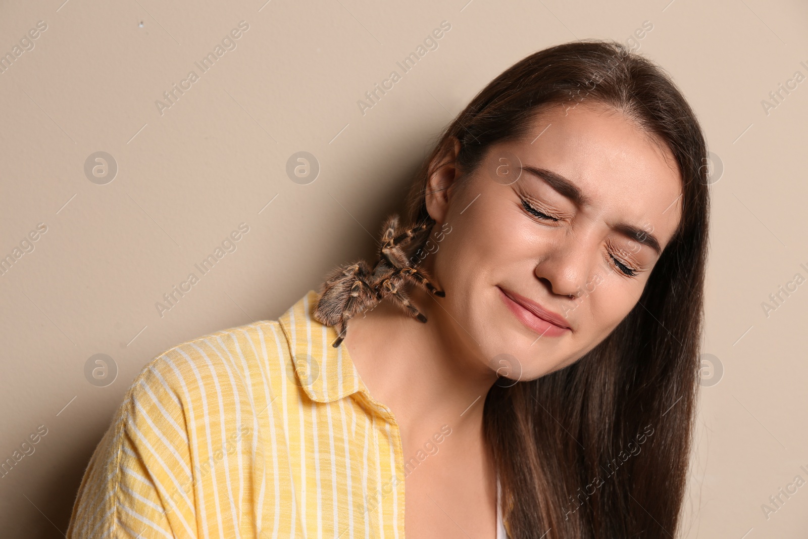 Photo of Scared young woman with tarantula on beige background. Arachnophobia (fear of spiders)