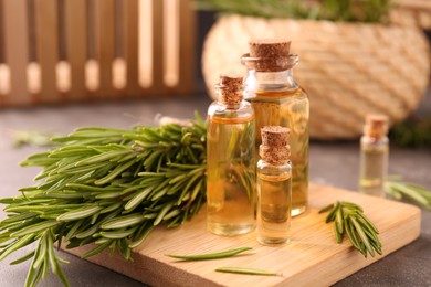 Photo of Essential oil in bottles and rosemary on grey table