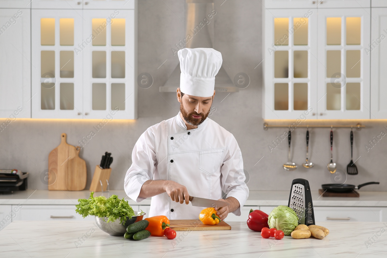 Photo of Chef cutting bell pepper at marble table in kitchen