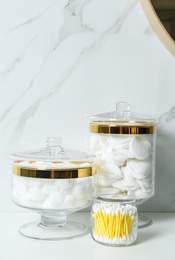 Photo of Jars with cotton balls, swabs and pads on white countertop in bathroom