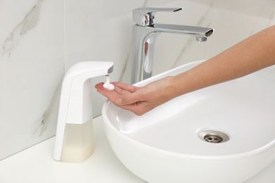 Woman using automatic soap dispenser in bathroom, closeup