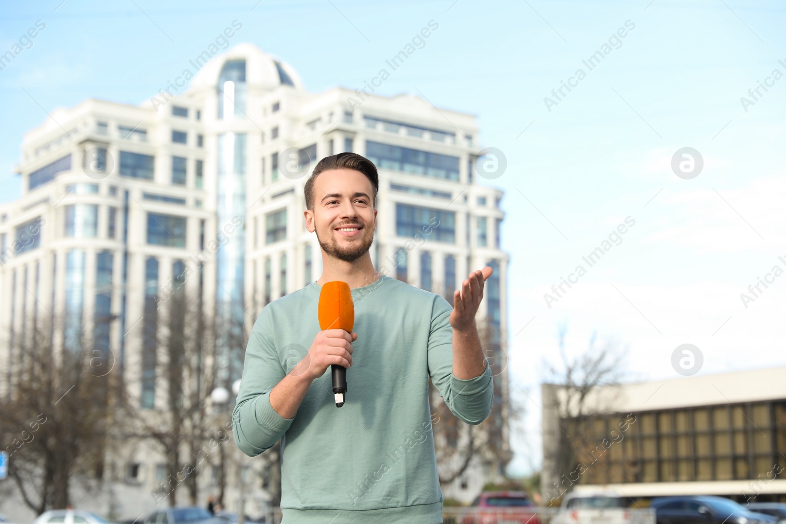 Photo of Young male journalist with microphone working on city street