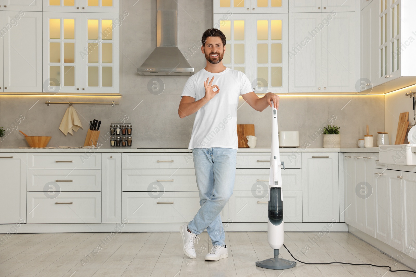 Photo of Happy man with steam mop showing ok gesture in kitchen at home
