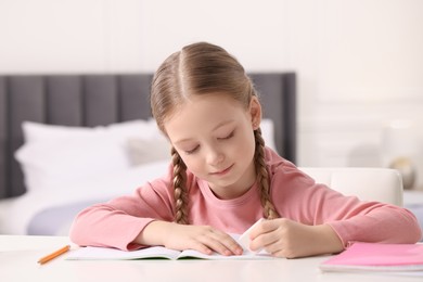 Girl using eraser at white desk in room