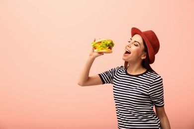 Photo of Young woman eating tasty burger on color background. Space for text