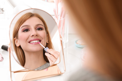 Beautiful young woman applying makeup near mirror indoors