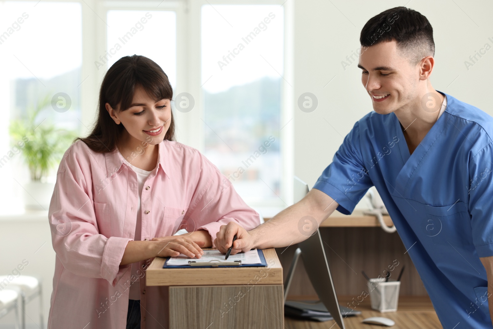 Photo of Smiling medical assistant working with patient at hospital reception