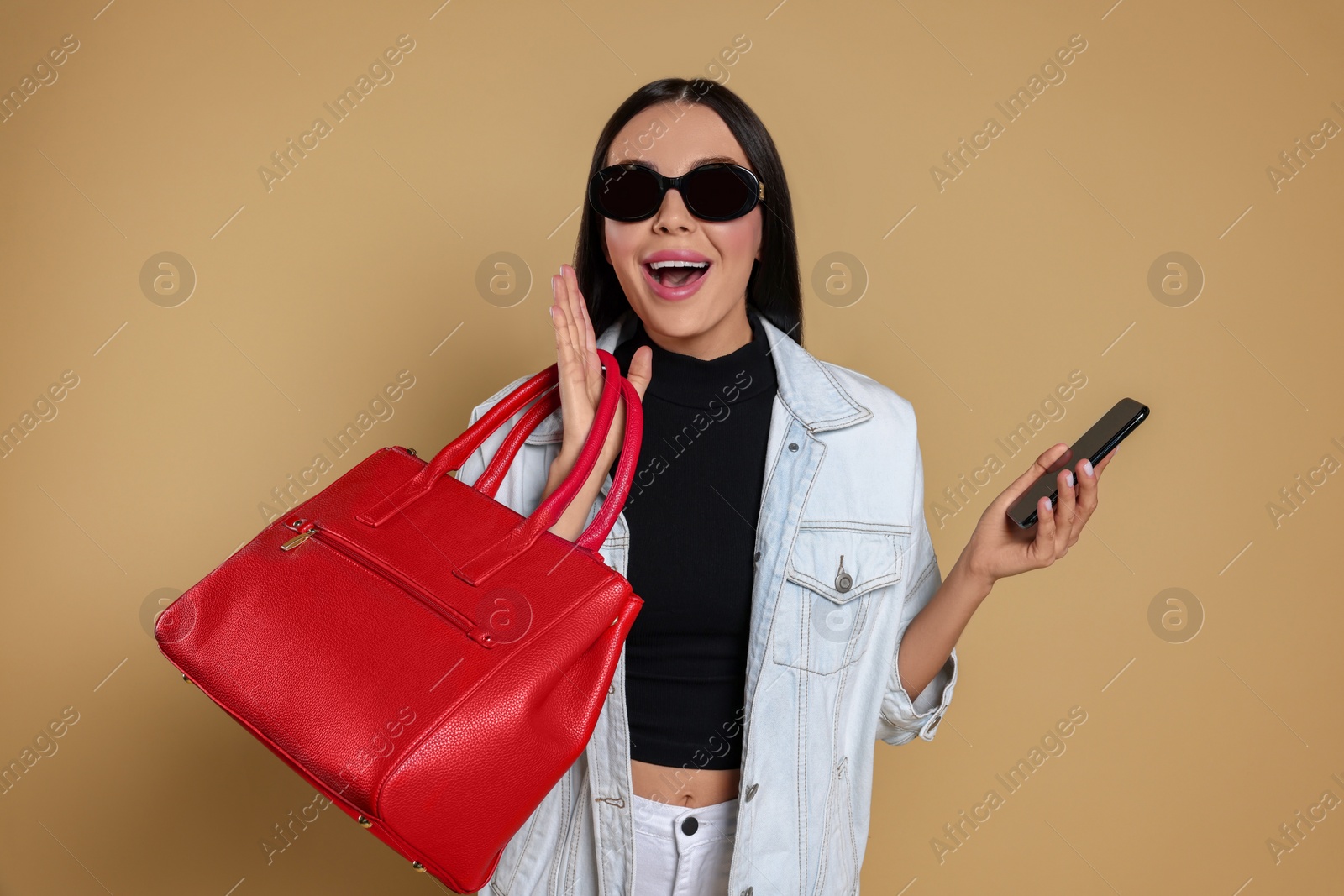 Photo of Emotional woman with stylish bag and smartphone on beige background