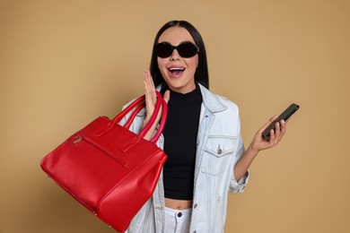 Photo of Emotional woman with stylish bag and smartphone on beige background