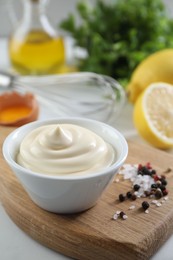 Tasty mayonnaise sauce in bowl, ingredients and spices on white table, closeup