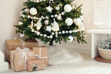 Photo of Decorated Christmas tree with faux fur skirt and gift boxes indoors, closeup