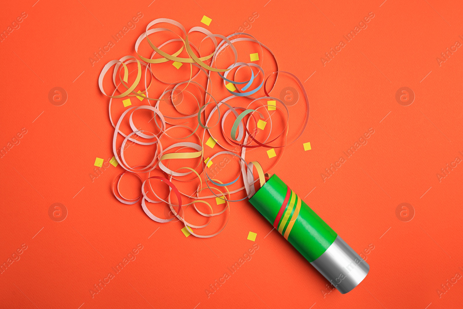 Photo of Beautiful serpentine and confetti bursting out of party popper on orange background, flat lay