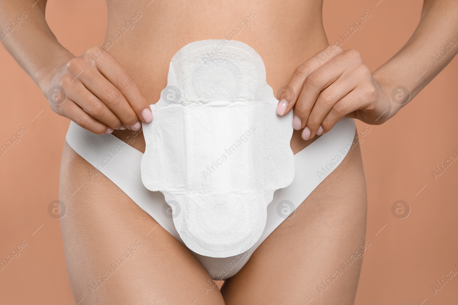 Photo of Woman in white panties with menstrual pad on peach background, closeup