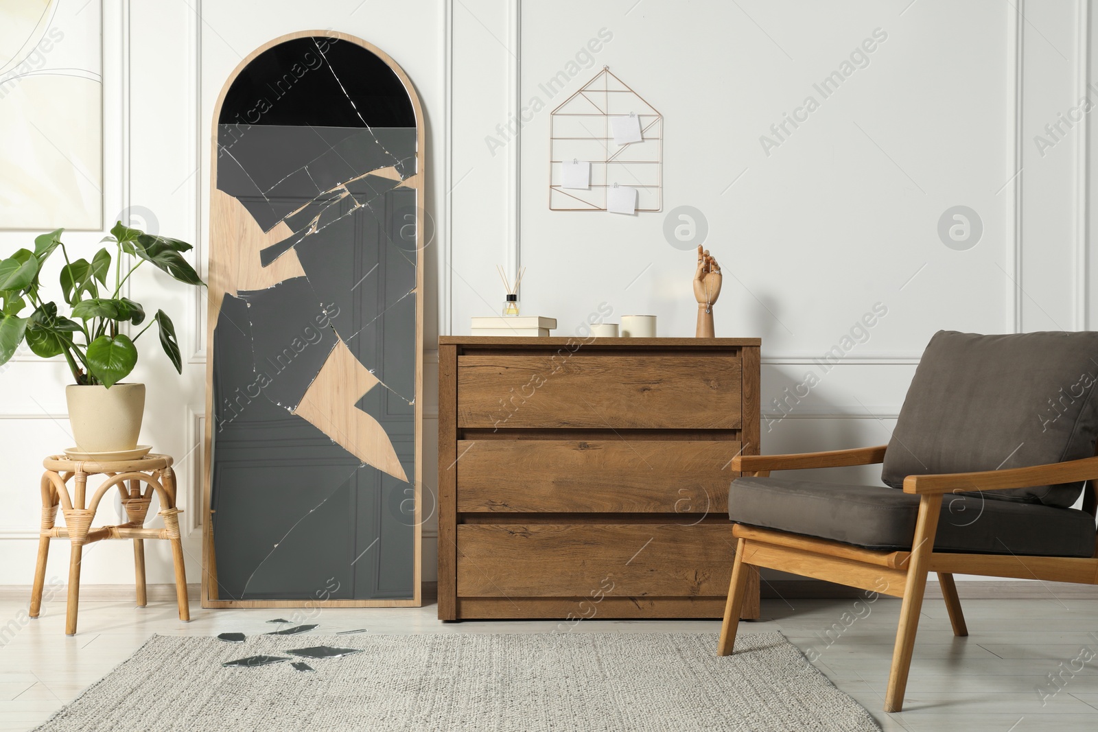Photo of Broken mirror, wooden chest of drawers, armchair and houseplant in room