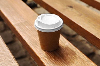 Takeaway paper cup with hot coffee on wooden bench outdoors