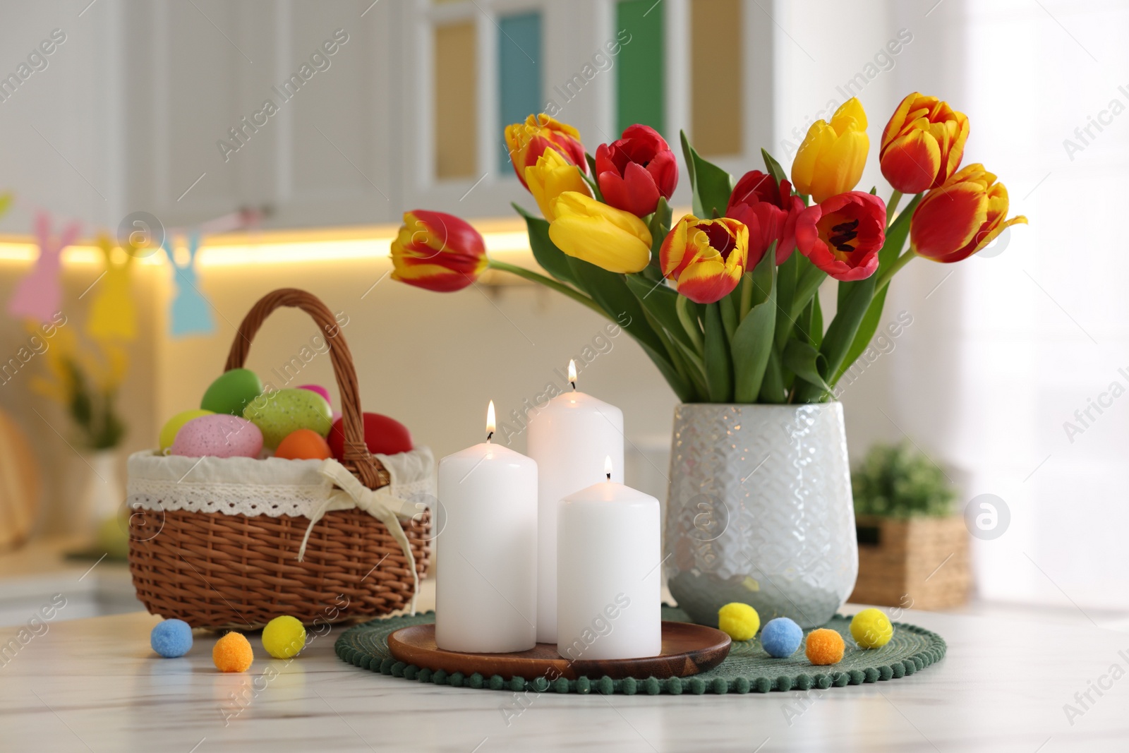 Photo of Easter decorations. Bouquet of tulips, painted eggs and burning candles on table indoors, closeup