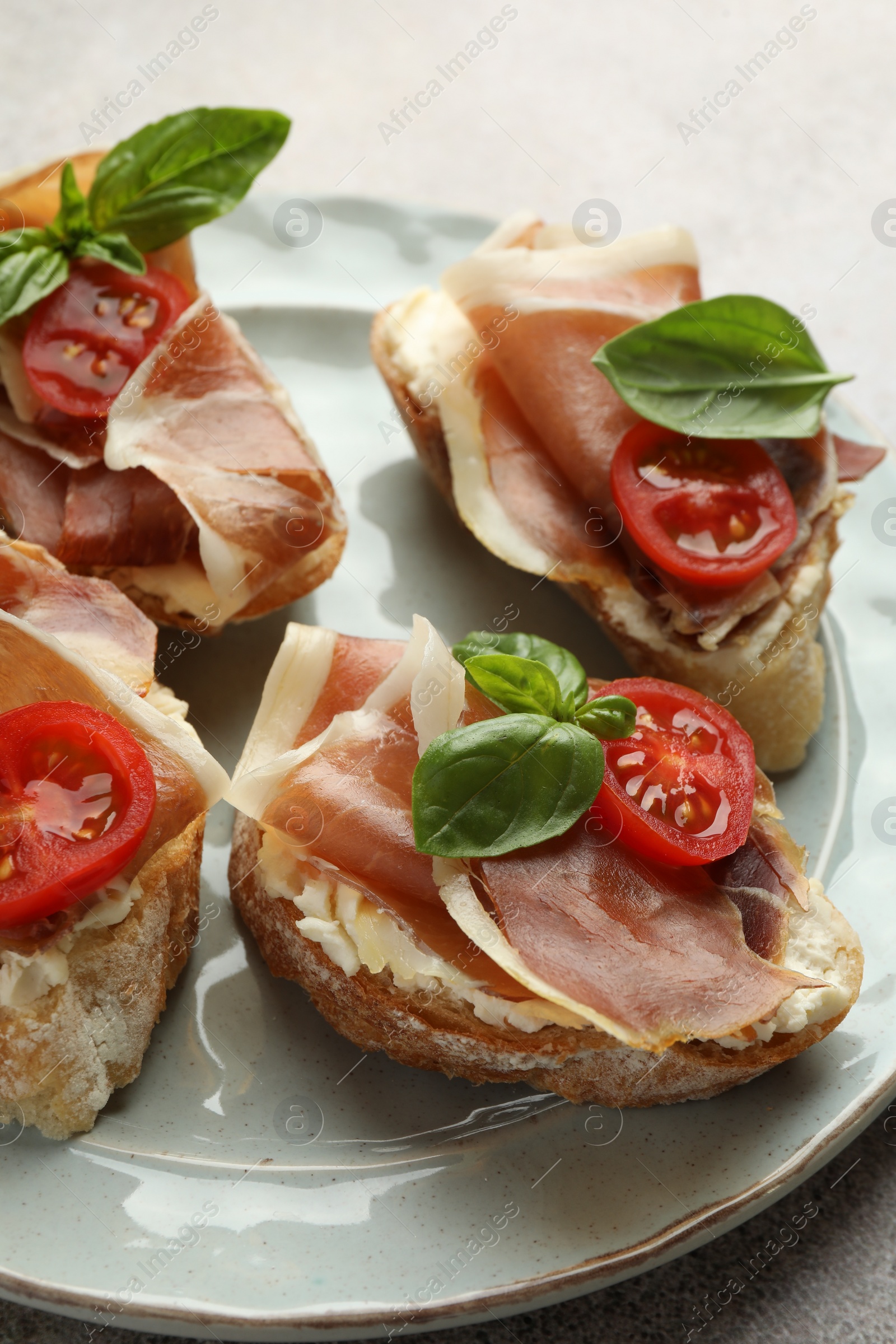 Photo of Tasty sandwiches with cured ham, basil and tomatoes on plate, closeup