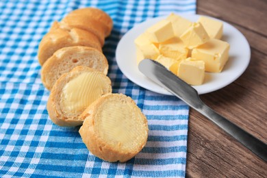 Photo of Tasty cut baguette with fresh butter on wooden table, closeup