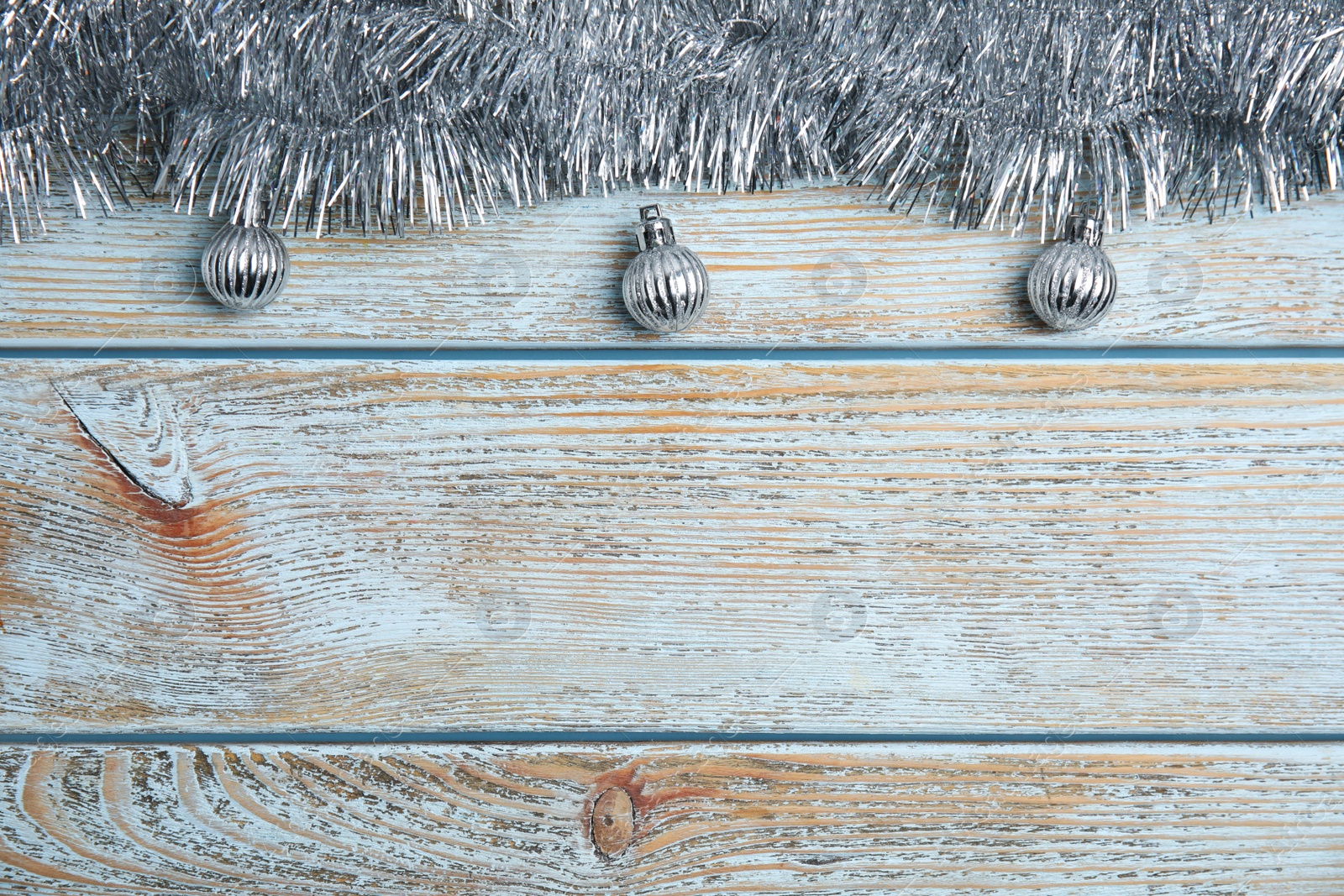 Photo of Silver tinsel and Christmas balls on light blue wooden background, flat lay. Space for text