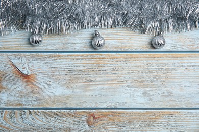 Silver tinsel and Christmas balls on light blue wooden background, flat lay. Space for text