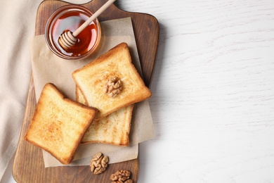 Photo of Tasty toasts served with honey and walnuts on white wooden table, flat lay. Space for text