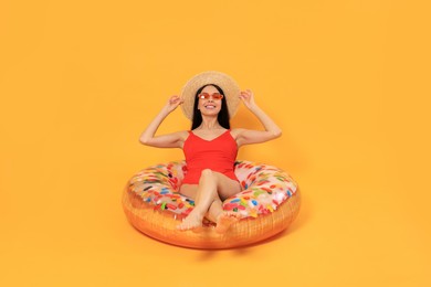 Photo of Happy young woman with beautiful suntan, hat and sunglasses on inflatable ring against orange background