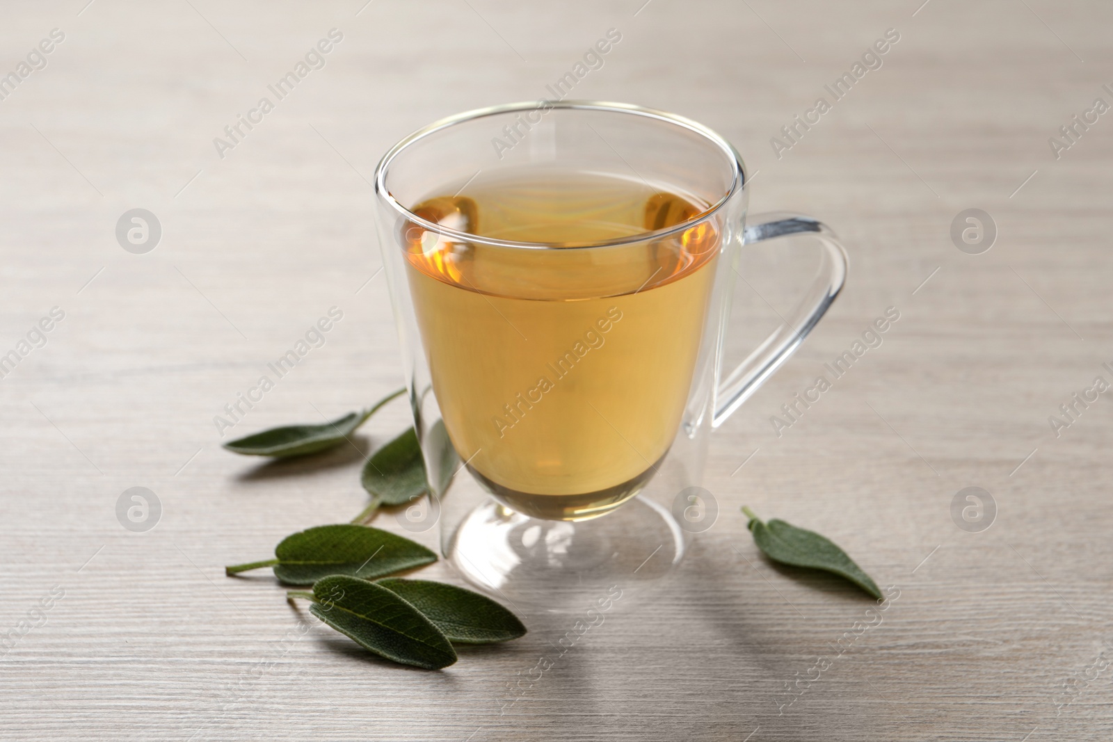 Photo of Glass cup of sage tea and green leaves on wooden table