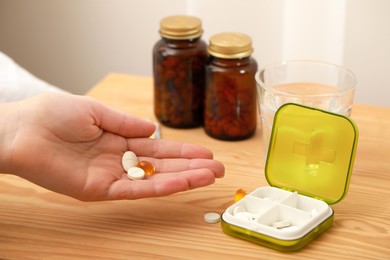 Woman taking pills from plastic box at wooden table, closeup