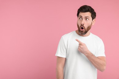 Surprised man pointing at something on pink background, space for text