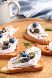 Photo of Tasty sandwiches with cream cheese, rosemary and berries on wooden tray, closeup