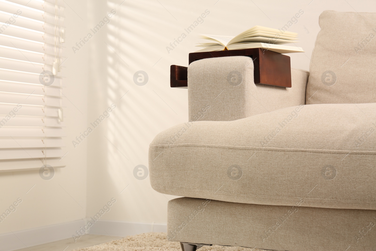 Photo of Open book on sofa with wooden armrest table in room, space for text. Interior element
