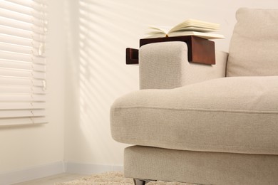 Open book on sofa with wooden armrest table in room, space for text. Interior element