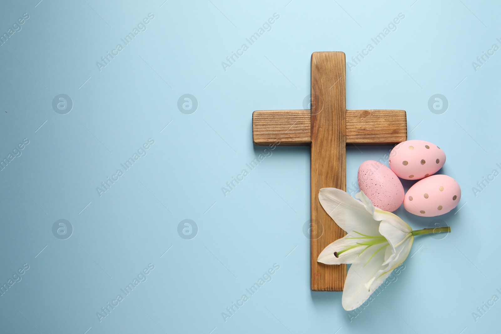 Photo of Wooden cross, painted Easter eggs and lily flower on light blue background, top view. Space for text