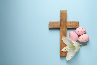 Wooden cross, painted Easter eggs and lily flower on light blue background, top view. Space for text