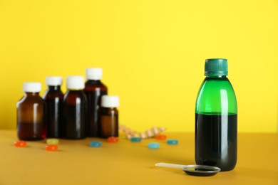 Photo of Bottle of cough syrup and dosing spoon on yellow background. Space for text