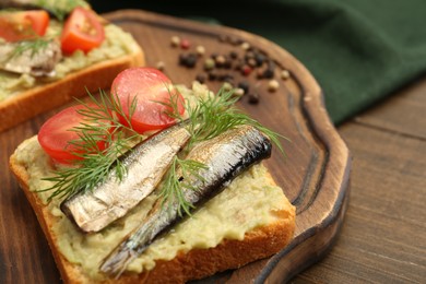 Photo of Delicious sandwich with sprats, tomato, dill and avocado puree on wooden table, closeup. Space for text
