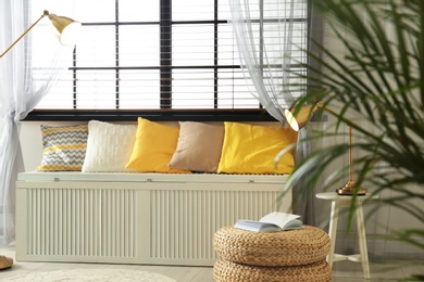 Wooden chest with pillows near window in room. Interior design