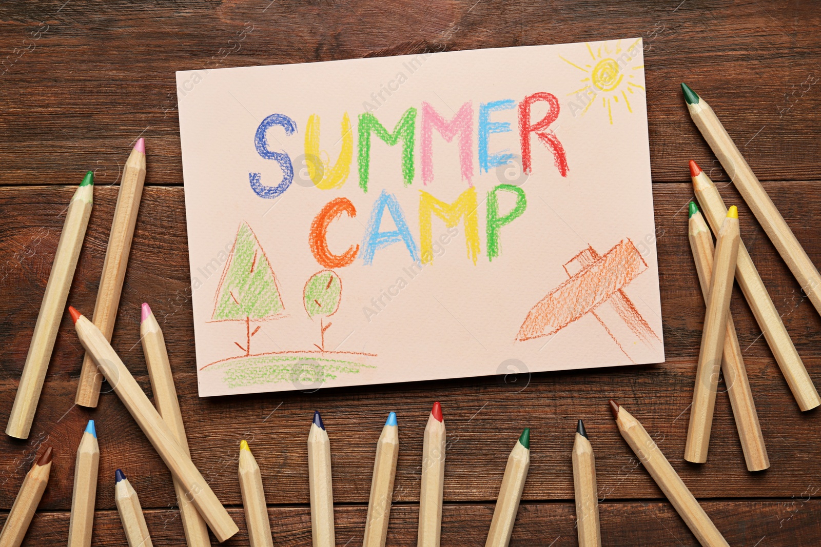 Photo of Card with text SUMMER CAMP, drawings and colorful pencils on wooden table, flat lay