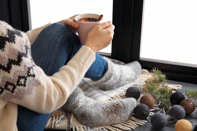 Woman relaxing with hot winter drink near window. Cozy season