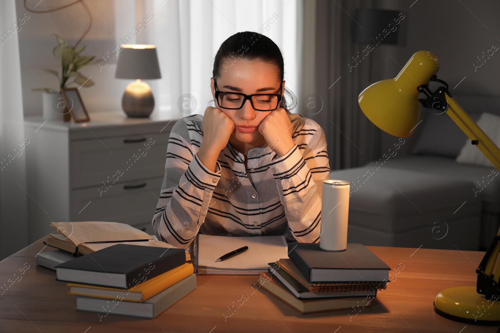 Photo of Tired young woman with energy drink studying at home