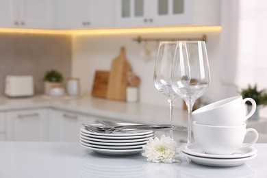 Photo of Set of clean dishware, glasses, cutlery and flower on table in kitchen, space for text