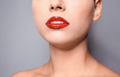 Photo of Beautiful young woman with red glossy lips on gray background, closeup