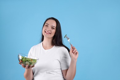 Beautiful overweight woman eating salad on light blue background, space for text. Healthy diet