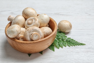 Bowl with fresh champignon mushrooms on wooden background, space for text